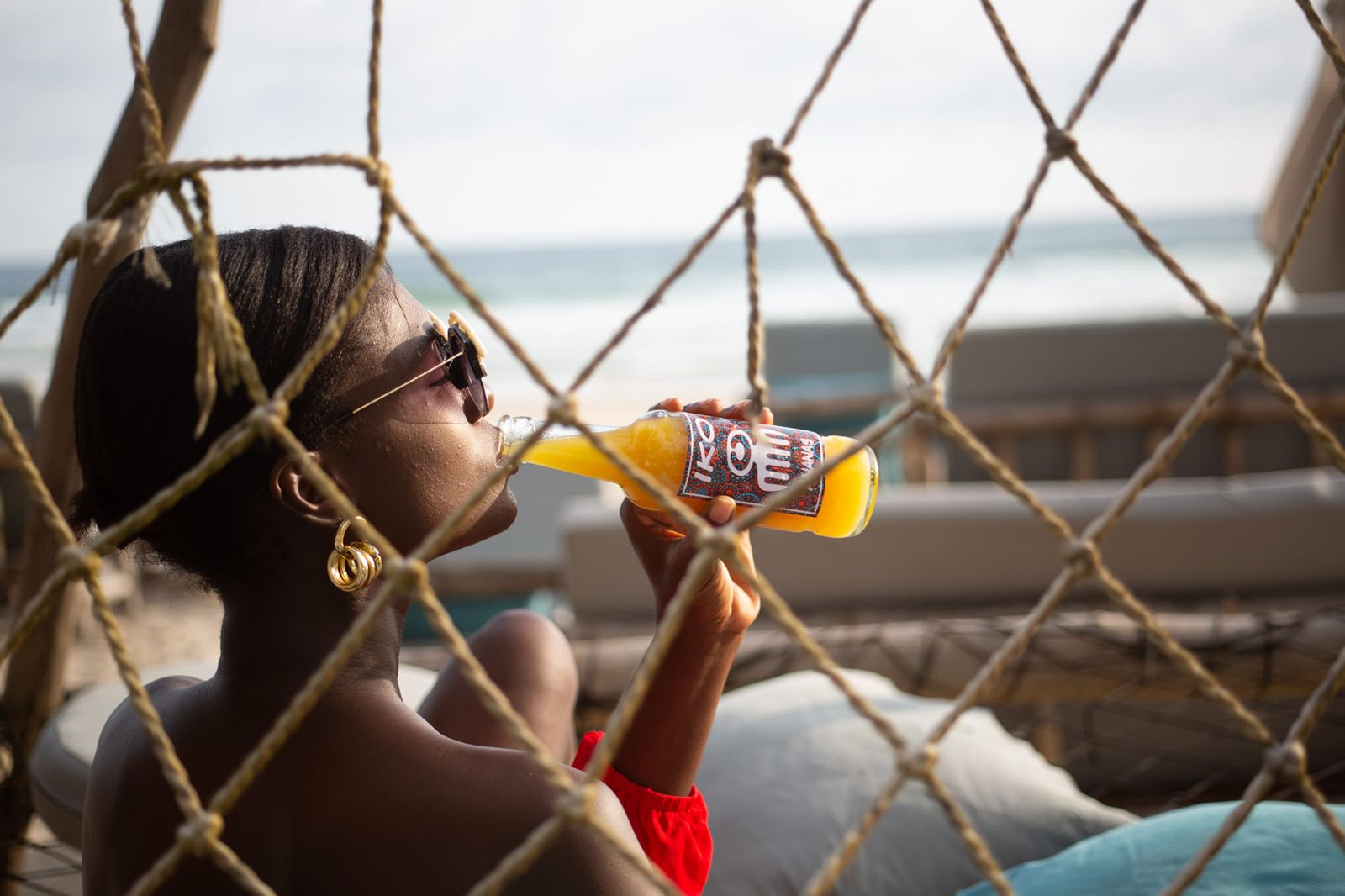Une femme boit un jus, allongée derrière un filet face à la mer